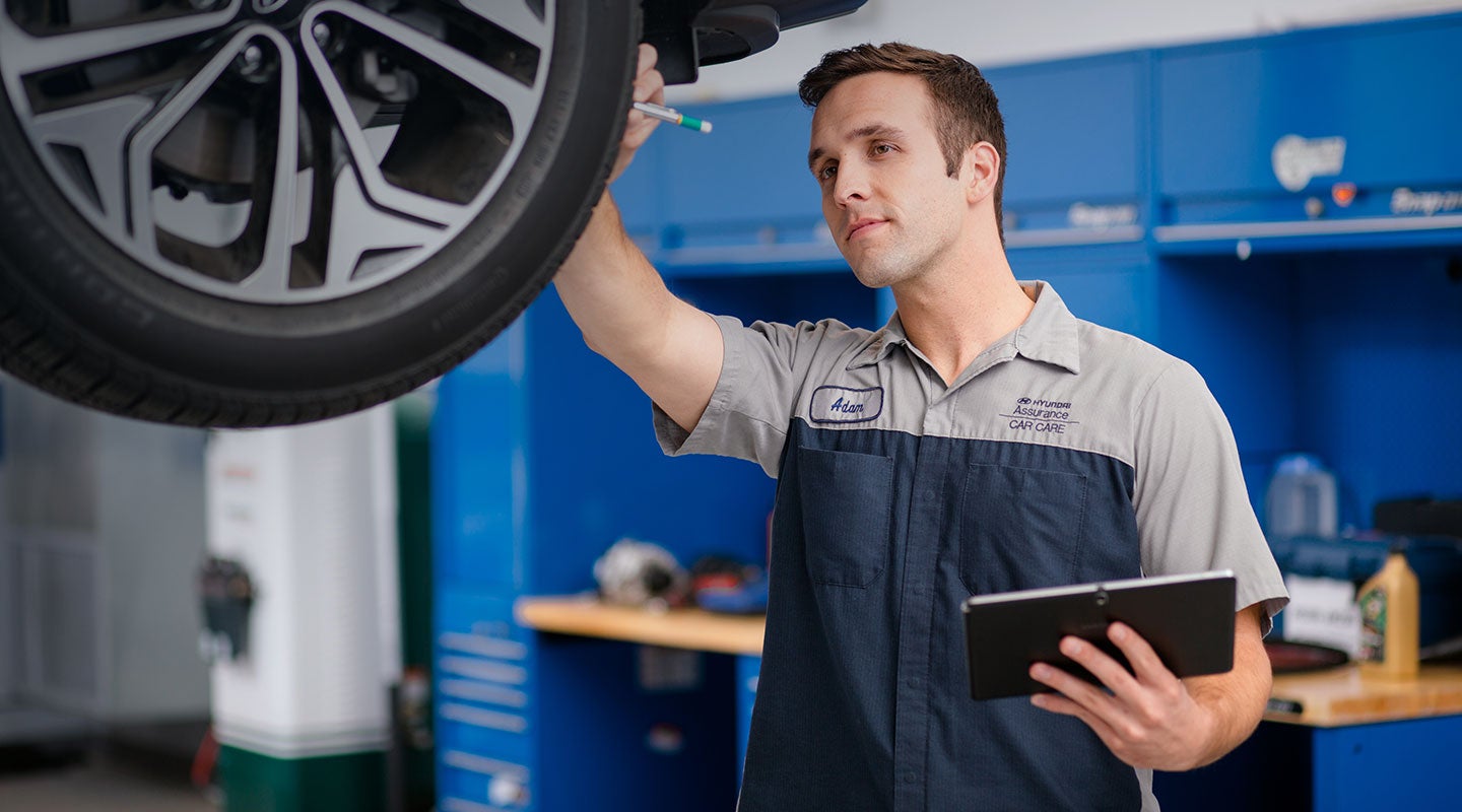 Hyundai-certified technician inspecting a tire on a lift in the Holler Hyundai service center